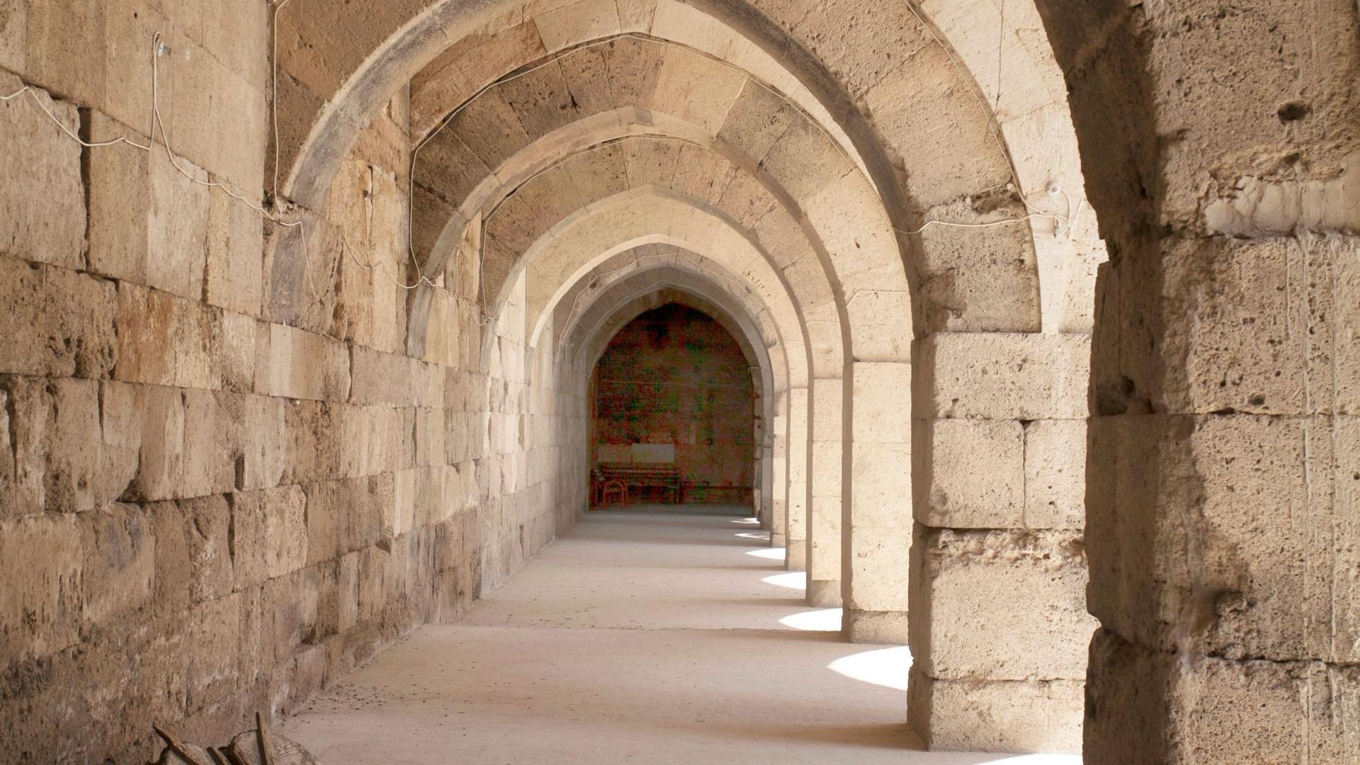 A long stone corridor of arches, lit from openings along one side.